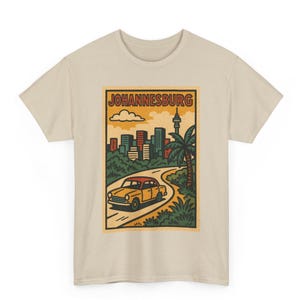 May include: Beige t-shirt featuring a vintage-style illustration of Johannesburg. The graphic includes a yellow car driving on a road, a cityscape, palm trees, and the text "JOHANNESBURG" in a rectangular frame. The design has a retro aesthetic.