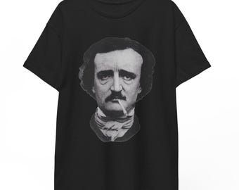 May include: Black t-shirt displaying a monochrome portrait of Edgar Allan Poe with a cigarette. The image is centrally placed, highlighting the author's face and upper torso. The t-shirt is suspended from a wooden hanger.