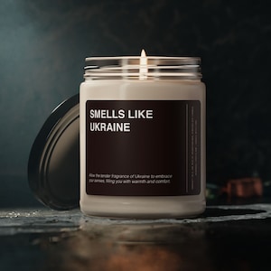 May include: A white candle in a glass jar with a black label that reads "SMELLS LIKE UKRAINE". The label also includes the text "Allow the tender fragrance of Ukraine to embrace your senses, filling you with warmth and comfort."