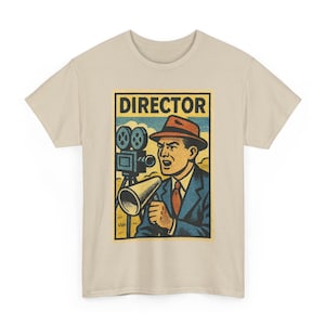 May include: Beige t-shirt featuring a retro-style graphic of a film director. The graphic includes a vintage film camera, a megaphone, and the word "DIRECTOR" in bold letters. The director is wearing a suit and hat.