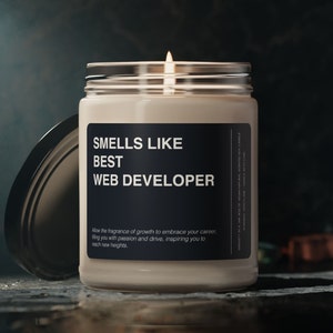 Könnte beinhalten: Eine weiße Kerze mit einem schwarzen Etikett, auf dem "Smells Like Best Web Developer" steht. Das Etikett enthält auch den Text "Allow the fragrance of growth to embrace your career, filling you with passion and drive, inspiring you to reach new heights."