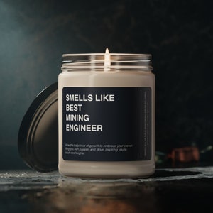 Pode incluir: Uma vela perfumada acesa num frasco de vidro com tampa prateada. O rótulo diz "SMELLS LIKE BEST MINING ENGINEER" em texto branco sobre fundo preto. O texto da vela também inclui a frase "Allow the fragrance of growth..."