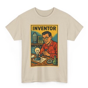 May include: Beige t-shirt featuring a retro-style graphic of an inventor. The image shows a man in a red shirt, glasses, and a lab coat, working on a lightbulb. The word "INVENTOR" is at the top of the graphic.