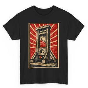 Può includere: T-shirt nero con grafica in stile xilografia di una ghigliottina. La ghigliottina è raffigurata in marrone e beige su uno sfondo rosso e beige a forma di raggiera. Il disegno è centrato sulla maglietta.
