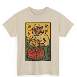 May include: Beige t-shirt featuring a colorful illustration of a beekeeper. The graphic shows a person in a bee suit holding a honeycomb frame, with bees buzzing around a hive. The design has a vintage, hand-drawn style.