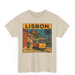 Puede incluir: Camiseta beige con una ilustración de estilo retro de un tranvía amarillo y rojo en Lisboa. La imagen incluye la palabra "LISBON" en naranja, edificios, una palmera y una persona caminando.