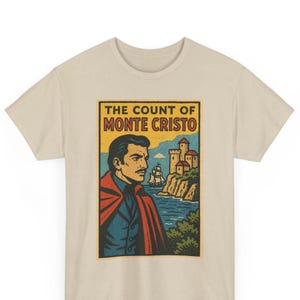 May include: A beige t-shirt with a vintage graphic from "The Count of Monte Cristo." The design shows a man in a red cape, a coastal scene with a castle, and the title in bold text. The shirt is made of a soft material.