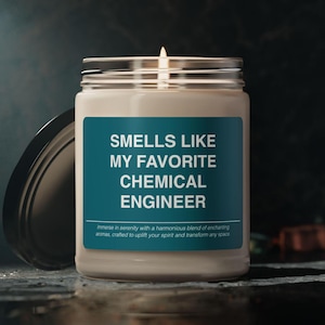 May include: A white candle with a teal label that reads "Smells Like My Favorite Chemical Engineer". The label also includes the text "Immerse in serenity with a harmonious blend of enchanting aromas, crafted to uplift your spirit and transform any space."