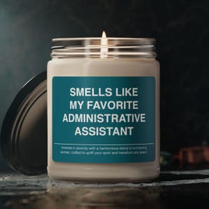 Puede incluir: Un tarro de vela azul verdoso con una etiqueta blanca que dice "Smells Like My Favorite Administrative Assistant". La etiqueta también incluye el texto "Immerse in serenity with a harmonious blend of enchanting aromas, crafted to uplift your spirit and transform any space."