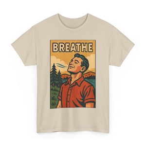 May include: Beige t-shirt featuring a retro-style graphic with the word "BREATHE" above an illustration of a person inhaling deeply in a natural setting. The person is wearing a red shirt, with a lake and trees in the background.