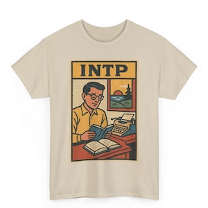 Può includere: T-shirt beige con grafica in stile retrò. La grafica include la parola "INTP" sopra un'illustrazione di una persona che legge un libro a una scrivania con una macchina da scrivere e una finestra che mostra un paesaggio.