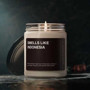 以下が含まれることがあります： 「SMELLS LIKE INDONESIA」と書かれた茶色のラベルが付いたガラス製のキャンドルジャー。ラベルには、「Allow the tender fragrance of Indonesia to embrace your senses, filling you with warmth and comfort.」というテキストも含まれています。