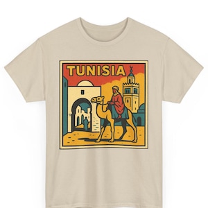 Könnte beinhalten: Beiges T-Shirt mit einem rechteckigen Grafikdesign mit dem Wort "TUNISIA" in Rot. Die Grafik zeigt eine Person auf einem Kamel, mit Gebäuden und einem Minarett im Hintergrund. Das Design hat einen Vintage-Reiseplakat-Stil.