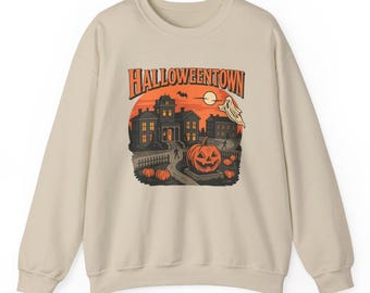 Peut inclure: Sweat-shirt beige avec un motif sur le thème d'Halloween. Le motif comprend une citrouille, des maisons hantées, un fantôme et le texte "Halloweentown" en orange. Le sweat-shirt a un col rond et des manches longues.