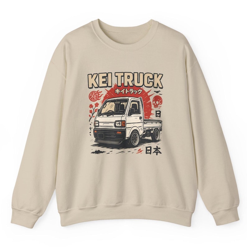Pu&ograve; includere: Felpa beige con una grafica di un camion Kei bianco. Il design include il testo "KEI TRUCK" in marrone, caratteri giapponesi, un sole rosso, un teschio e simboli giapponesi.