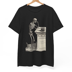May include: Black t-shirt featuring a detailed black and white illustration of a skeleton leaning on a stone pedestal. The skeleton is in a thoughtful pose, with its chin resting on its hand. The pedestal has text on it.