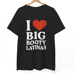 Op de afbeelding: Zwart T-shirt met de tekst "I ❤️ BIG BOOTY LATINAS" in het wit en een rode hartafbeelding. Het shirt hangt aan een houten hanger tegen een witte achtergrond. Het T-shirt is een casual kledingstuk.