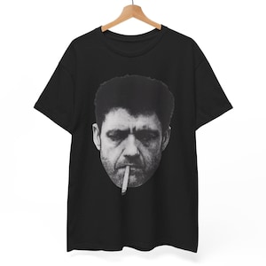 May include: Black t-shirt featuring a black and white image of a man with a cigarette in his mouth. The image is a close-up of the man's face. The t-shirt is hanging on a wooden hanger.
