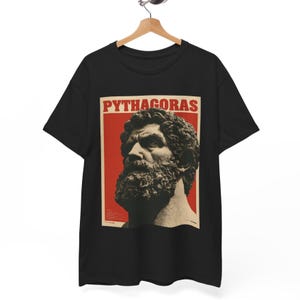 May include: A black short-sleeved t-shirt featuring a rectangular graphic print on the chest. The print displays a beige-toned bust of Pythagoras against a red background, with the text PYTHAGORAS in bold red capital letters at the top.