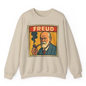 Może przedstawiać: Beżowa bluza z ilustracją w stylu retro przedstawiającą Zygmunta Freuda palącego fajkę. Obraz jest oprawiony w czerwony baner z napisem "FREUD". Grafika jest w stylu vintage komiksu, z odważnymi liniami i ograniczoną paletą kolor&oacute;w.