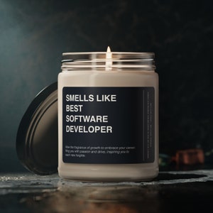 May include: A white candle in a glass jar with a black label that reads "Smells Like Best Software Developer". The label also includes the text "Allow the fragrance of growth to embrace your career, filling you with passion and drive, inspiring you to reach new heights."