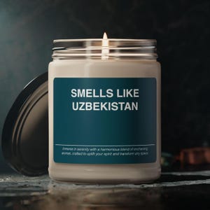 Peut inclure: Une bougie blanche dans un pot en verre avec une étiquette bleu sarcelle qui indique "SMELLS LIKE UZBEKISTAN". L'étiquette comprend également le texte "Immerse in serenity with a harmonious blend of enchanting aromas, crafted to uplift your spirit and transform any space."