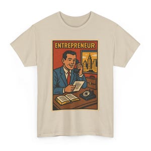 May include: Beige t-shirt featuring a retro-style graphic of a man in a suit talking on the phone. The graphic includes the word "ENTREPRENEUR" in a red box, a cityscape, and a vintage telephone.