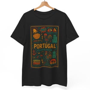 Puede incluir: Camiseta negra con un diseño gráfico colorido que muestra la palabra "PORTUGAL" y varias ilustraciones. El diseño incluye un gallo, una campana, un castillo y otros símbolos, con el texto "ATLANTIC OCEAN" y "LISBON".
