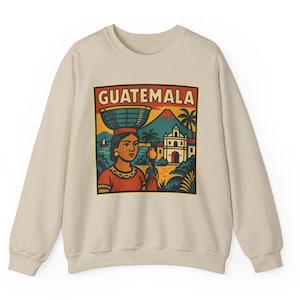 May include: Cream-colored sweatshirt featuring a colorful graphic of a woman carrying a basket on her head, with the word "GUATEMALA" above. The design includes a volcano, church, and palm trees.