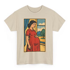 May include: Beige t-shirt featuring a pop art style illustration of a pregnant person in a red dress looking out a window. The window shows a blue sky, clouds, and a green tree. The illustration is framed in a black border.