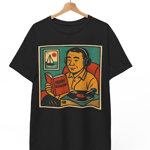 Puede incluir: Camiseta negra con una ilustración retro de un hombre leyendo un libro titulado "Haruki Murakami" y escuchando música en un tocadiscos. El diseño incluye una pequeña pintura de un velero y una puesta de sol.