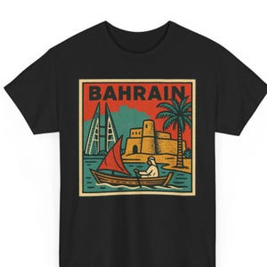 May include: Black t-shirt featuring a vintage-style graphic of Bahrain. The design includes a boat, a fort, palm trees, and the word "BAHRAIN" in bold letters. The artwork is set against a red, teal, and yellow background.