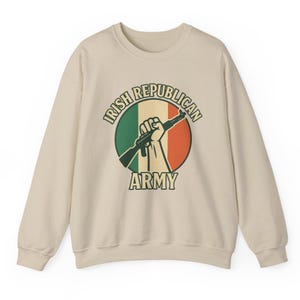 May include: A beige sweatshirt featuring a circular graphic with the text "IRISH REPUBLICAN ARMY." The graphic includes a hand holding a rifle, set against a green, white, and orange background, resembling the Irish flag.