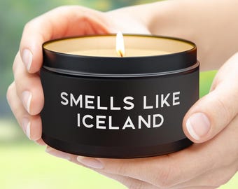 May include: A black candle with a white label that reads "Smells Like Iceland". The candle is lit and the wax is a light yellow color.