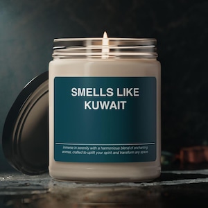 May include: A white candle in a glass jar with a teal label that reads "SMELLS LIKE KUWAIT". The label also includes the text "Immerse in serenity with a harmonious blend of enchanting aromas, crafted to uplift your spirit and transform any space."