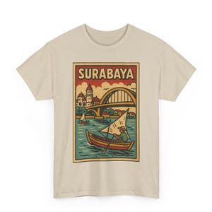 Könnte beinhalten: Beiges T-Shirt mit einer Illustration im Vintage-Stil von Surabaya. Das Design zeigt ein Boot auf dem Wasser, eine Brücke und den Stadtnamen in einem rechteckigen Rahmen. Die Grafik ist in Braun-, Orange- und Blautönen gehalten.