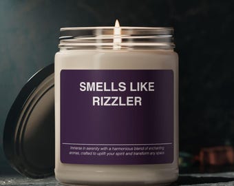Puede incluir: Un tarro de vidrio para velas con una etiqueta morada que dice "SMELLS LIKE RIZZLER". La vela está encendida y el tarro está sobre una superficie oscura.