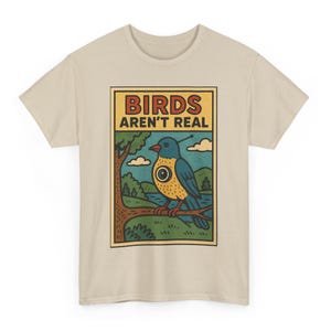 May include: Beige t-shirt with a rectangular graphic featuring a cartoon bird with a camera eye, perched on a branch. The text "BIRDS AREN'T REAL" is above the bird. The bird is blue, yellow, and red.