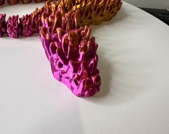 May include: A pink and gold 3D printed snake sculpture with a spiky texture. The snake is curled up in a coil shape.