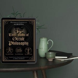 Może przedstawiać: Tablet cyfrowy wyświetla okładkę książki "Three Books of Occult Philosophy" autorstwa Heinricha Corneliusa Agrippy. Okładka jest czarno-złota z ilustracjami. Zielony ceramiczny dzbanek i filiżanka stoją na ciemnym drewnianym stole, wraz z małym notatnikiem.