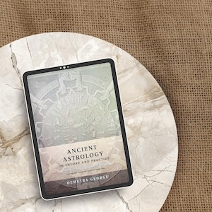 May include: A digital tablet displaying the book "Ancient Astrology in Theory and Practice" by Demetra George. The tablet is on a marble-patterned surface, set against a textured, tan background.