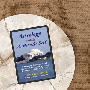 May include: A book titled "Astrology and the Authentic Self" on a marble surface. The cover features the title in blue, with a photo of a white building by the water. The author's name is Demetra George.