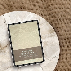 May include: A digital tablet displaying the cover of a book titled "Ancient Astrology in Theory and Practice." The cover features a beige illustration with text in a dark brown band. The tablet rests on a marble-patterned surface against a burlap background.