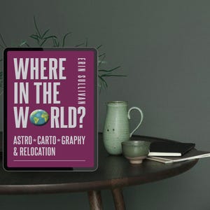 May include: A tablet displays the text "WHERE IN THE WORLD?" in white, with "ASTRO * CARTO * GRAPHY & RELOCATION" below. The tablet is on a dark wooden table with a green ceramic vase, a small cup, and a notebook.