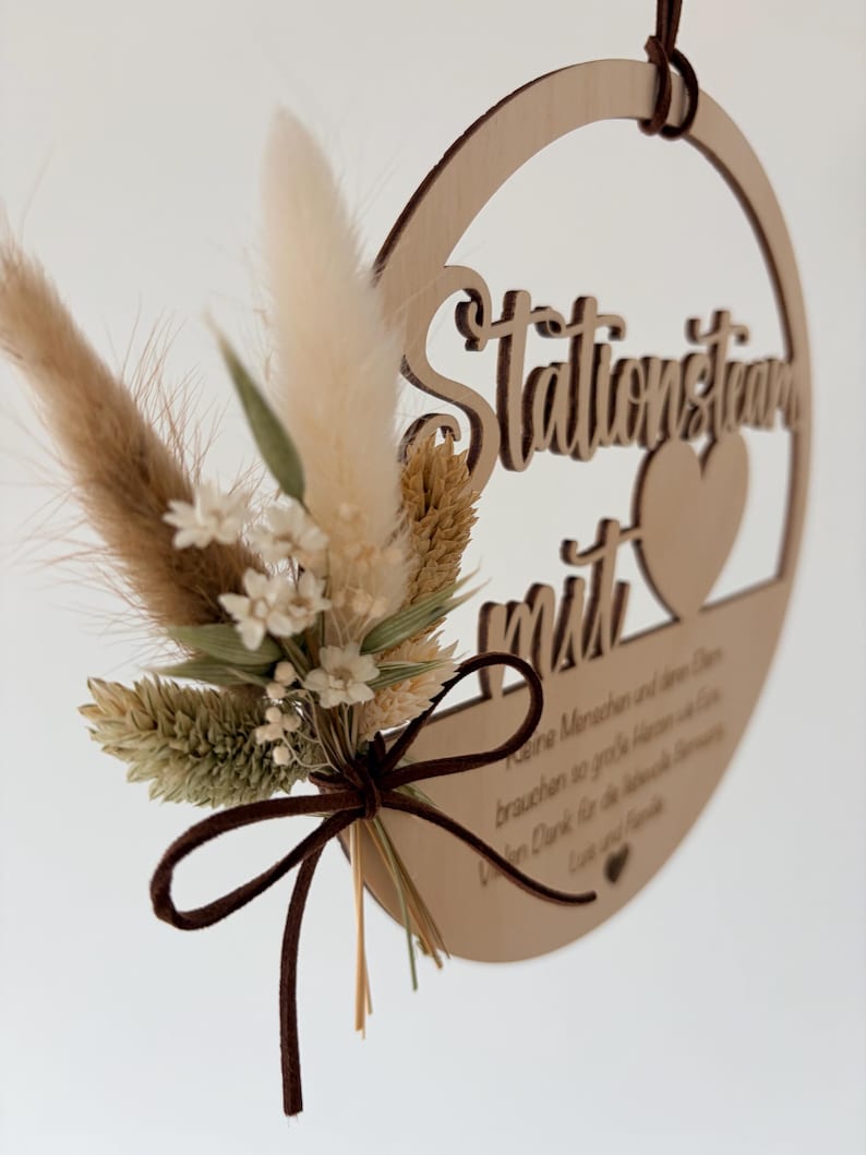 May include: A wooden circular sign with the words "Stationstraum mit" and a heart cutout. The sign is adorned with dried flowers and tied with a brown ribbon. A brown leather cord is attached for hanging.