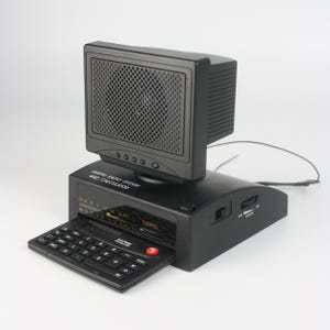 Könnte beinhalten: Ein schwarzes Radiowecker mit integriertem Taschenrechner. Das Radio hat einen Lautsprecher oben und einen herausziehbaren Taschenrechner. Der Text "AM/FM RADIO SYSTEM AND CALCULATOR" ist auf der Vorderseite aufgedruckt.