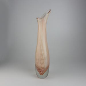 May include: A tall, elegant glass vase with a slender, elongated shape. The vase features a clear base that transitions to a body with vertical, cream-colored stripes and reddish-orange accents. The top curves gracefully to one side.
