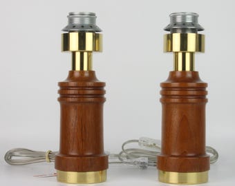 May include: A pair of wooden table lamps with brass accents. The lamps are cylindrical in shape and have a textured wood finish. Each lamp has a brass ring at the top and a silver metal shade.