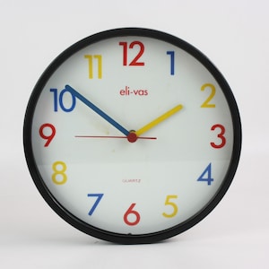 Reloj de pared Eli-vas vintage de los años 80. Cuarzo alemán, 22 cm. Marco de metal negro y cristal. Estilo Memphis. Decoración retro colorida.