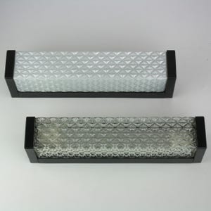 Può includere: Due applique da parete rettangolari con un pannello di vetro strutturato a motivo diamantato incastonato in una cornice nera. Le applique sono progettate per l'illuminazione interna e hanno un'estetica moderna.